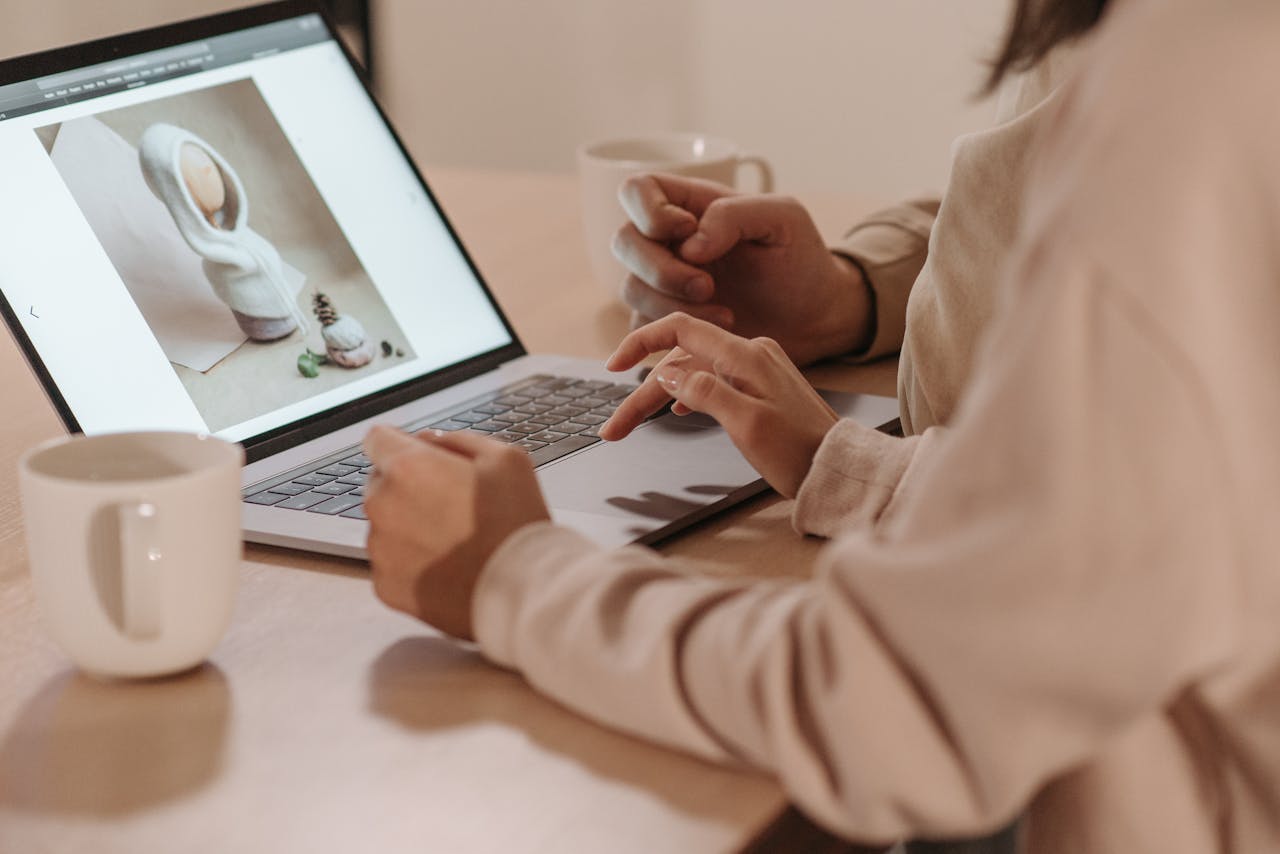 Two individuals reviewing a photo on a laptop, enjoying coffee indoors.
